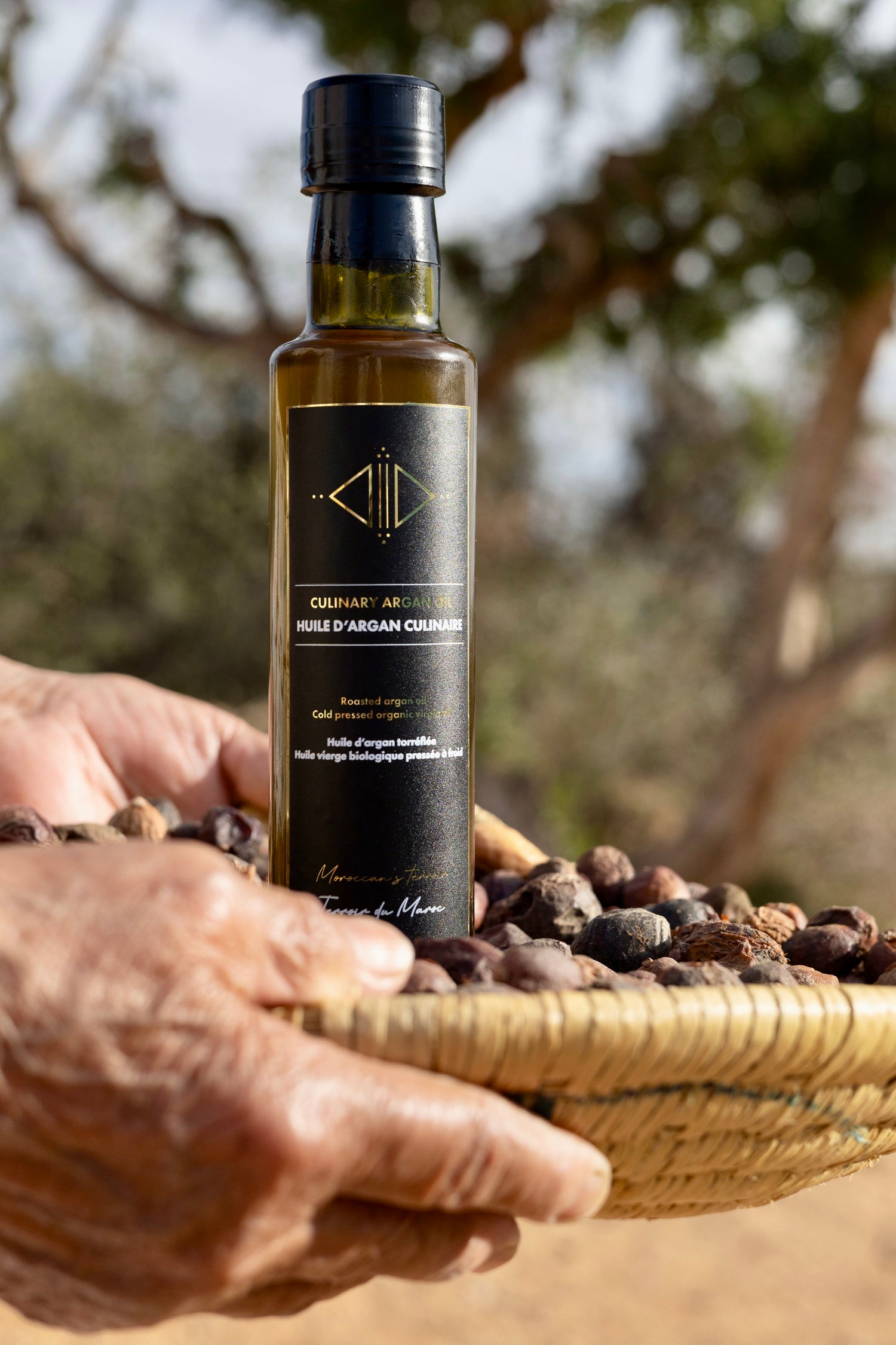 A Moroccan woman's hand gently holding pure argan oil, with the traditional bottle nearby, showcasing the timeless craftsmanship and heritage of argan oil production in Morocco